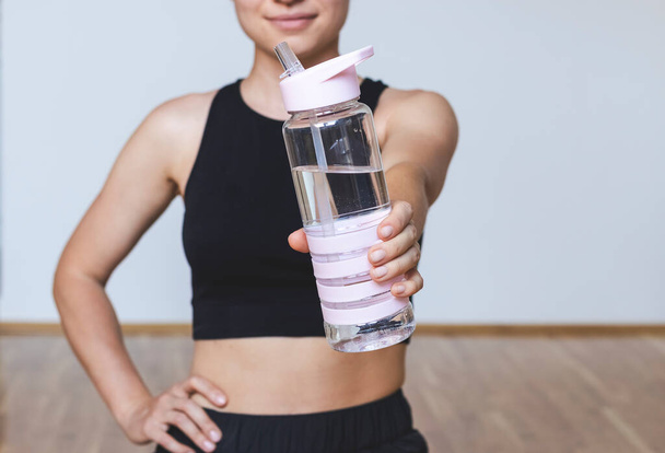 Mujer en forma sostiene una botella de agua en sus manos delante de ella. - Foto, Imagen