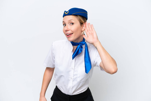 Avión mujer azafata rubia aislada sobre fondo blanco escuchando algo poniendo la mano en la oreja - Foto, imagen