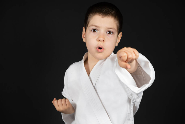Küçük bir çocuk dövüş sanatları yapıyor. Kimono karate dersleri alıyor. Siyah bir arka planda.. - Fotoğraf, Görsel