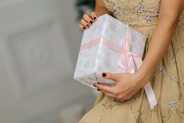 Primer plano de las manos femeninas sosteniendo hermoso regalo de Navidad con cinta rosa sobre fondo blanco - Foto, Imagen
