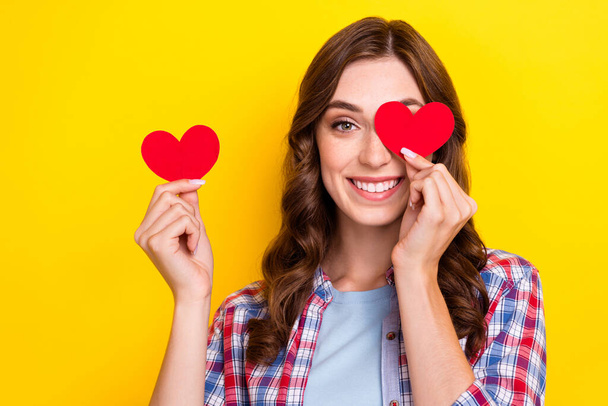 Closeup photo of young pretty woman cover eye red paper love symbol toothy smiling enjoy her new boyfriend isolated on yellow color background. - Фото, изображение