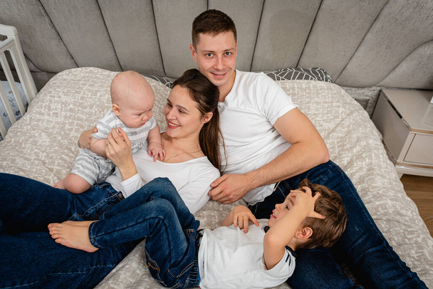  Young, emotional, cheerful, big family, mom, dad and sons lie on a big bed and look at the camera. - Foto, Imagen