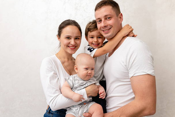 portrait of a young family, father, mother and two small sons, cheerful, friendly and strong family. They smile and hug children in their arms. The concept of a young friendly family  - Foto, Imagen