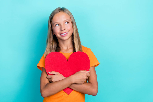 Photo of little dreamy schoolgirl kid hug her big red paper heart positive looking interested youtube blog channel empty space isolated on cyan color background. - Fotografie, Obrázek