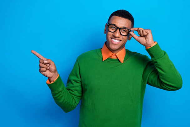 Portrait of cheerful positive guy orange shirt under green pullover directing empty space touch eyewear isolated on blue color background. - Foto, Imagen