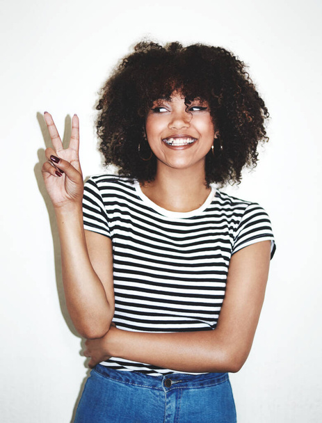 Peace, sign and black woman with smile, excited and casual against a gray studio background. Young female, hand gesture and girl being silly, goofy and playful with trendy, edgy and stylish look - Fotografie, Obrázek