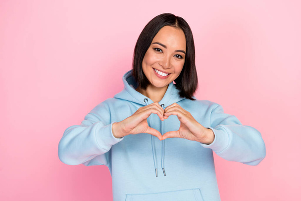 Photo of cheerful pretty girl dressed blue sweatshirt smiling showing arms heart isolated pink color background. - Foto, afbeelding