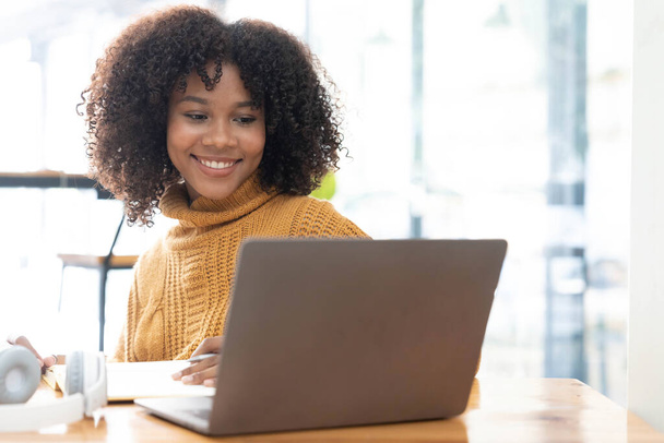 Zdjęcie wesołej radosnej mieszanej rasy kobieta w żółtej koszuli uśmiechnięta praca na laptopie rozmawiać wideo rozmowy online. Inteligentna etniczna kobieta w słuchawkach uczy się zdalnie na komputerze w domu. Koncepcja edukacji... - Zdjęcie, obraz