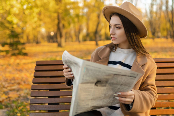 Atrakcyjna dziewczyna czyta gazetę w parku. Prywatny detektyw nadzorujący obiekt. Atrakcyjny agent wywiadu..  - Zdjęcie, obraz