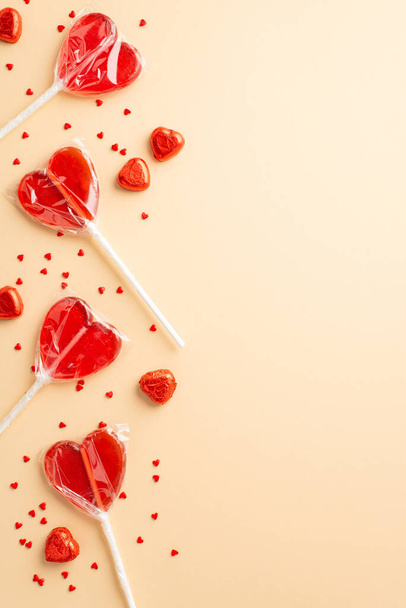 Концепция Дня Святого Валентина. Вертикальный вид фото сердечной формы леденцы шоколадные конфеты и конфетти на изолированном бежевом фоне с копипространством - Фото, изображение