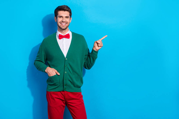 Photo of funny cheerful guy dressed xmas green cardigan pointing finger empty space isolated blue color background. - Foto, Imagem