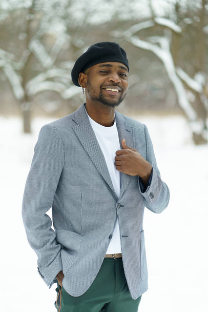 Proud african guy smile staying across snow in park Young man hold on jacket. High quality photo - Photo, Image
