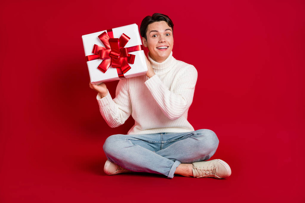 Full size photo of cheerful excited person sitting floor hands hold receive newyear giftbox isolated on red color background. - Foto, immagini