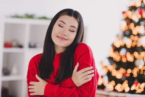 Portrait of nice pretty satisfied optimistic woman straight hairdo wear red knit pullover embrace herself eyes closed in house indoors. - Foto, imagen