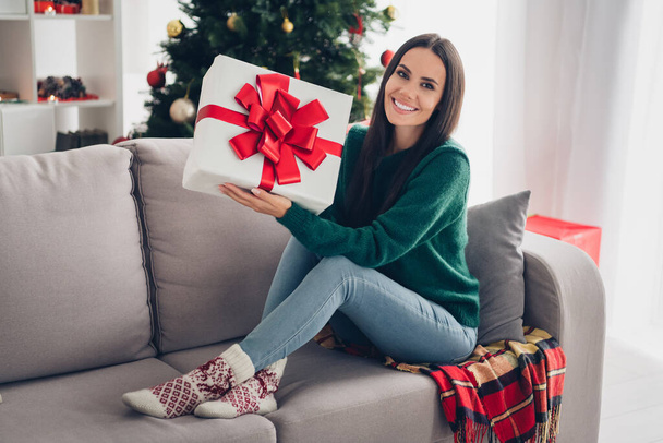 Photo of positive excited lady dressed knitted x-mas sitting couch rising present box indoors house room. - Foto, afbeelding