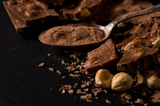 Broken chocolate nuts pieces and cocoa powder in spoon on dark background - Fotoğraf, Görsel