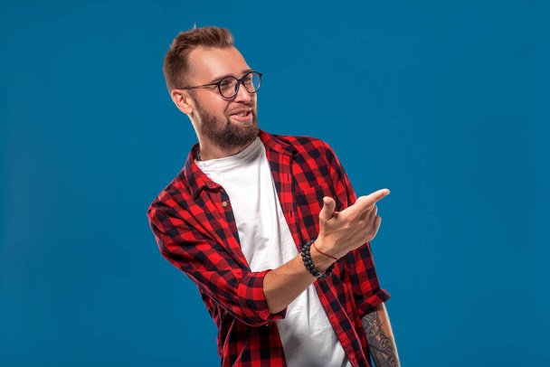 Emotional and people concept: young bearded man in checkered shirt. Hipster style. Studio shot on blue background. Copy space - Photo, Image
