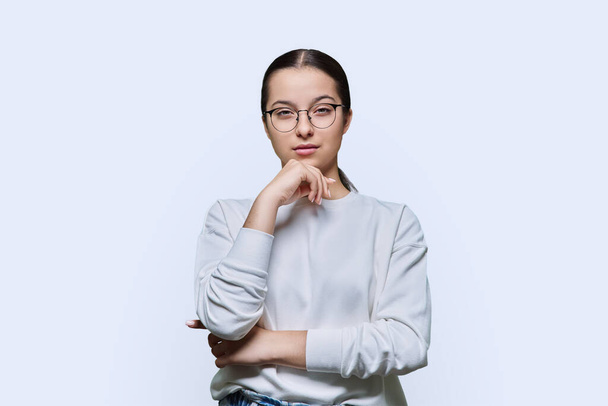 Teenage girl in glasses looking at camera on white studio background. Portrait of smart student teenager 14, 15 years old. Adolescence, high school, lifestyle emotions education concept - Foto, imagen