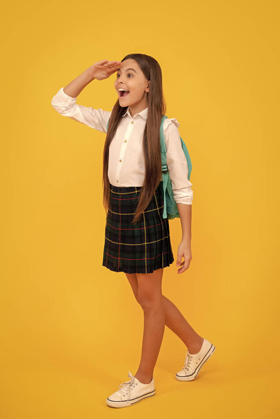 niño feliz con mochila en uniforme escolar longitud completa sobre fondo amarillo mirar lejos, escuela. - Foto, imagen