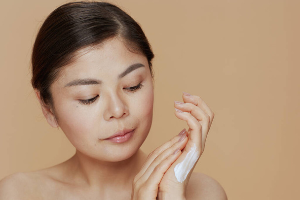 modern asian female with hand cream on beige background. - Foto, Bild