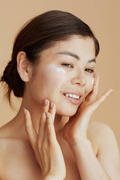 young asian female with facial cream on face against beige background. - Фото, зображення