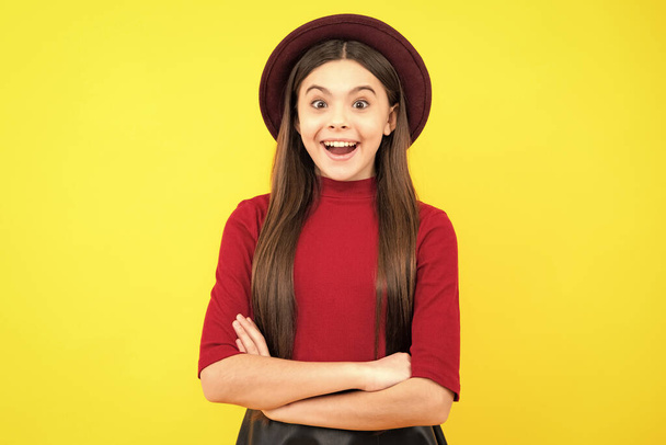 Happy teenager portrait. Smiling girl. Confident child keep arms crossed, isolated on yellow background, empty space. Little caucasian teenage girl 12, 13, 14 years old hold hands crossed - Valokuva, kuva