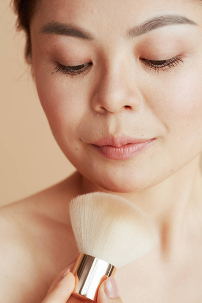 modern asian woman with makeup brush against beige background. - Fotoğraf, Görsel