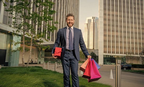 уверенный предприниматель в корпоративном костюме, держащий сумку и подарочную коробку за пределами офиса, женский день. - Фото, изображение