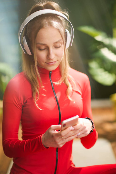 modern woman in red fitness clothes with headphones using smartphone in the modern green living room. - 写真・画像