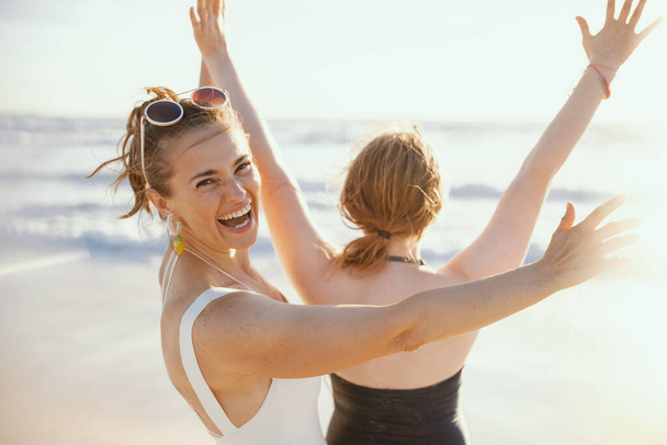 happy stylish mother and teenage daughter at the beach in swimsuit rejoicing. - Foto, Bild