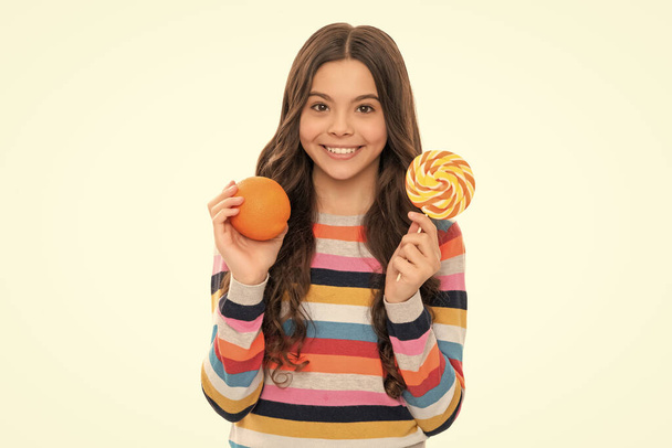 オレンジ色の果物とロリポップが白い、健康的な子供時代に隔離されたカラフルなセーターで幸せな子供. - 写真・画像