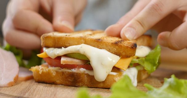 Ein Sandwich mit Schinken, Salat, reifen Tomatenscheiben und Käsestücken zubereiten. Fastfood-Konzept. - Foto, Bild