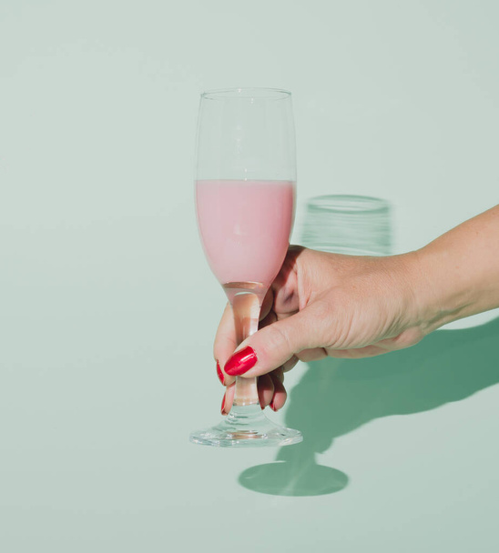 Жіноча рука тримає келих рожевого шампанського. Святковий настрій. Концептуальна обстановка на пастельному тлі
. - Фото, зображення