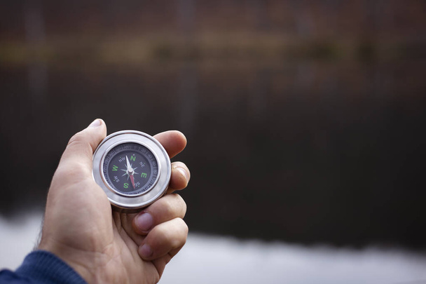 Holds a compass on the background of the lake during the day - Photo, Image