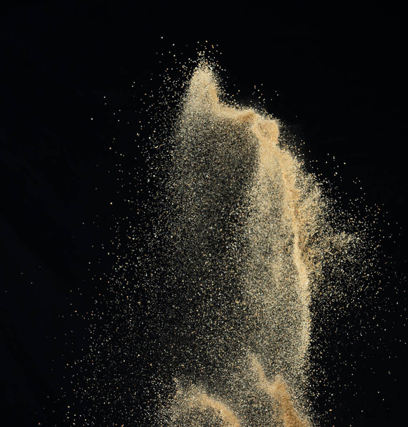 Sand flying explosion, Golden sand wave explode. Abstract sands cloud fly. Yellow colored sand splash throwing in Air. black background Isolated high speed shutter, throwing freeze stop motion - Foto, immagini