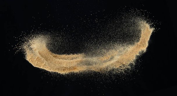 Sand flying explosion, Golden sand wave explode. Abstract sands cloud fly. Yellow colored sand splash throwing in Air. black background Isolated high speed shutter, throwing freeze stop motion - Photo, Image