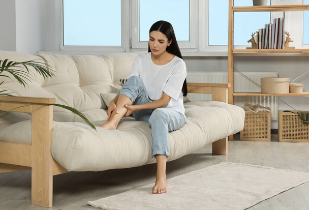 Young woman rubbing sore leg on sofa at home - Foto, immagini