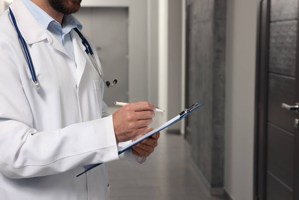 Doctor in white coat with stethoscope and clipboard indoors, closeup. Space for text - Photo, Image