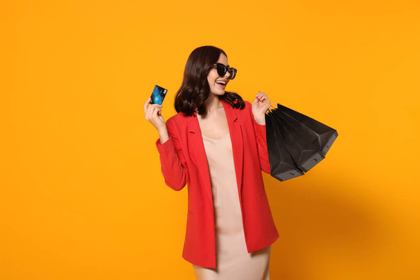 Beautiful young woman with paper shopping bags and credit card on yellow background - Fotoğraf, Görsel