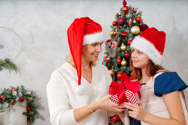 Smiling mother gives her daughter a christmas present. Happy family sharing joy with each other. Christmas day at home. Merry Christmas and Happy Holidays. Christmas holiday celebration - Photo, Image