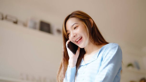 Счастливая молодая азиатка, говорящая по мобильному телефону дома, девушка-подросток отвечает на звонки по сотовому телефону, сидя на диване. Азиатка разговаривает на смартфоне - Фото, изображение