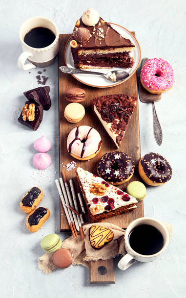 Selection of various cake pieces, macaroons, meringues, cookies and donuts on a wooden desk on a light background. Top view. Confectionery background. - Valokuva, kuva