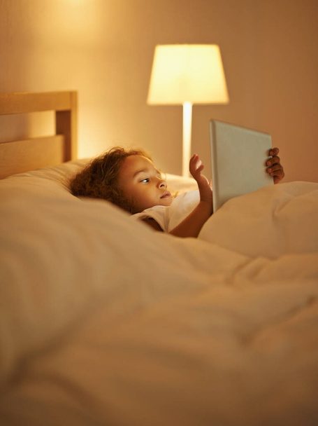 Elegir esta noche sueño. Una linda niña acostada en una cama doble y jugando en una tableta - Foto, imagen