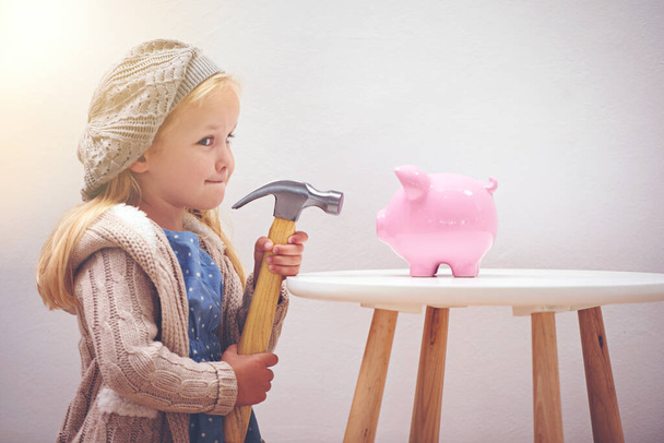 Verlockend, oder? Ein kleines Mädchen steht neben ihrem Sparschwein mit einem Hammer - Foto, Bild