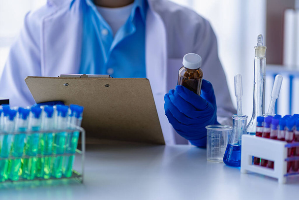Doktor bere zkumavku s modrou tekutinou, virolog pracuje v chemickém ochranném obleku člověk studuje nebezpečný virus Biolog na laboratorním stole s mikroskopem v laboratoři - Fotografie, Obrázek