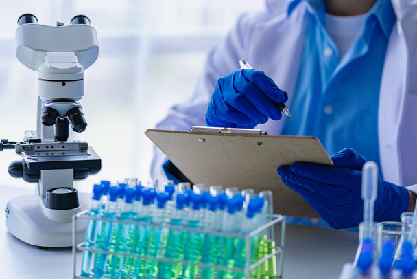 Arzt nimmt Reagenzglas mit blauer Flüssigkeit, Virologe im chemischen Schutzanzug studiert gefährlichen Virenbiologen am Labortisch mit Mikroskop im Labor - Foto, Bild