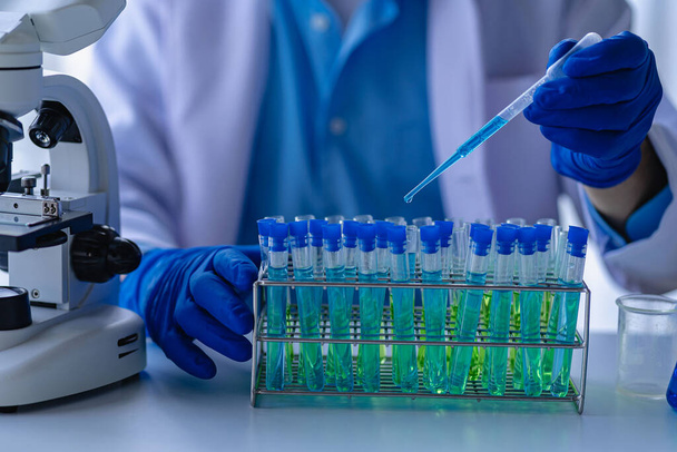 Dokter neemt reageerbuis met blauwe vloeistof, viroloog werkt in chemische beschermende pak man bestudeert gevaarlijke virus Bioloog aan de laboratoriumtafel met een microscoop in het laboratorium - Foto, afbeelding
