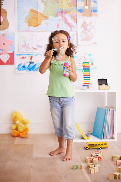 Blowing bubbles is a serious business. an adorable little girl blowing bubbles in her bedroom - Foto, Imagen