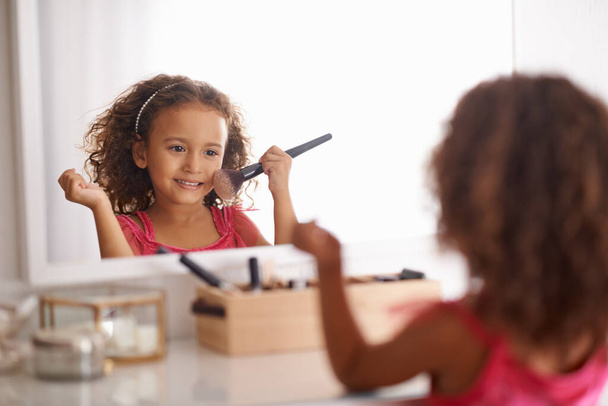 Aprender los entresijos de la belleza desde una edad temprana. una niña aplicando colorete en el espejo - Foto, imagen