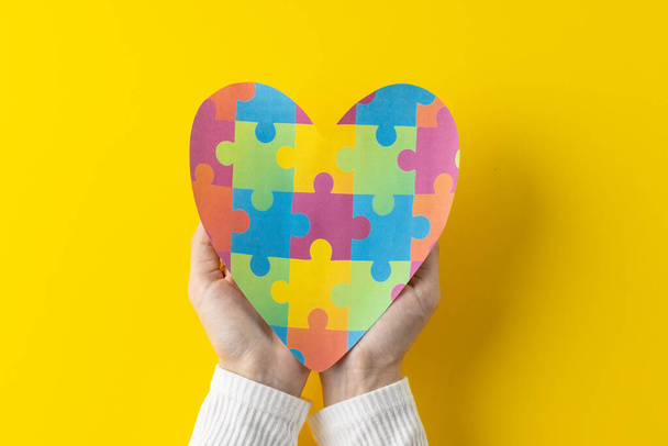 Composition of hands holding jigsaw puzzle heart on yellow background with copy space. Medical services, healthcare and health awareness concept. - Фото, изображение